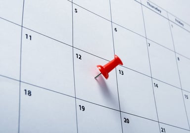 partial image of paper calendar with a red pin stuck on the 12th of the month