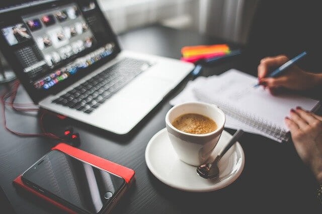 hand writing on pad of paper, coffee cup, laptop