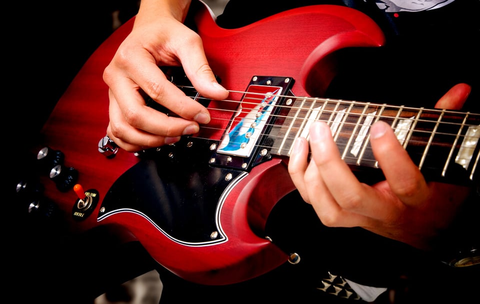 Hands playing a red electric guitar