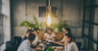 Blurred image of people meeting around a table. Focus on lightbulb near viewer.