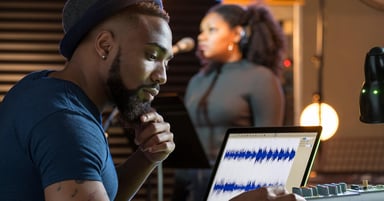 Man in front of computer with woman singing into a mic in the background