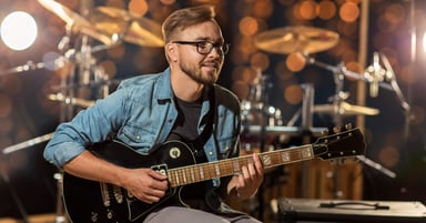 Young man with glasses and beard playing electric guitar