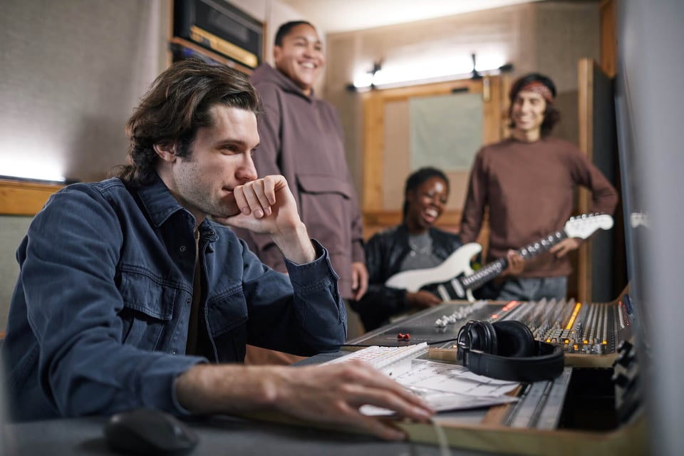 4 young adults in a recording studio, one playing guitar